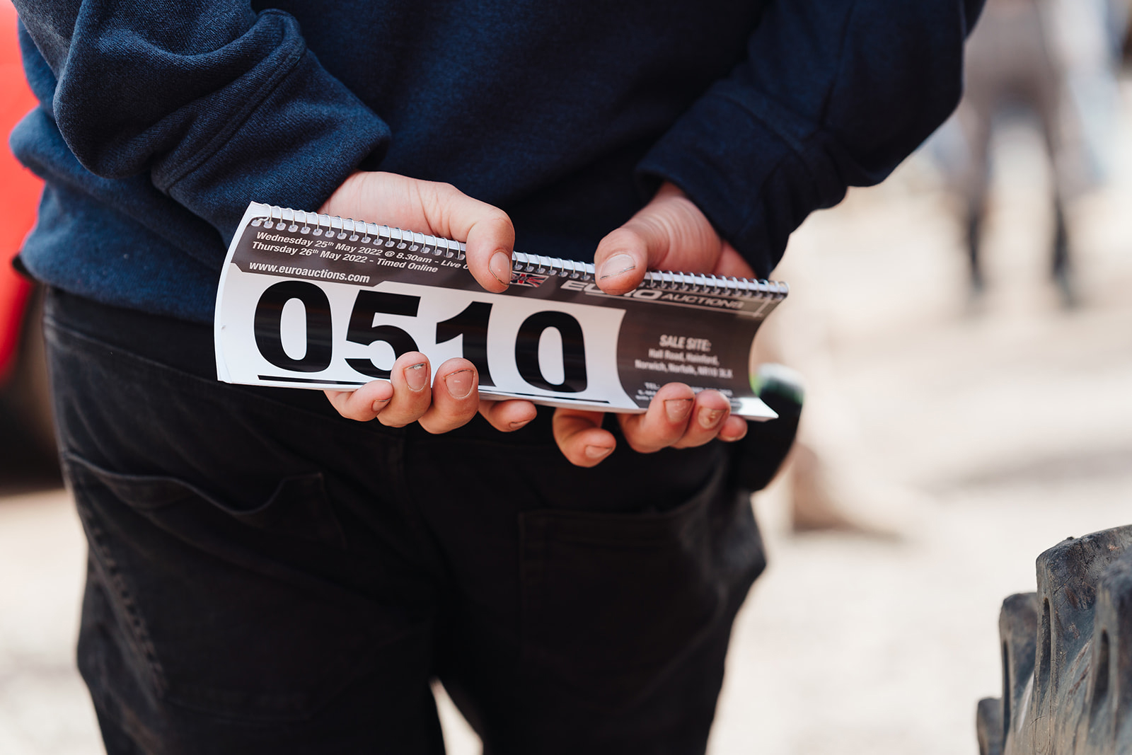 Persona que sostiene en sus manos el número de pujador tras su espalda